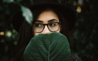 A woman wearing glasses is covering her face with a green leaf.