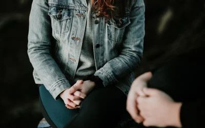 A woman in a denim jacket is sitting on a stool talking to a man.