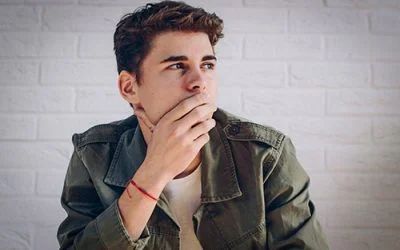 A young man in a green jacket is covering his mouth with his hand.