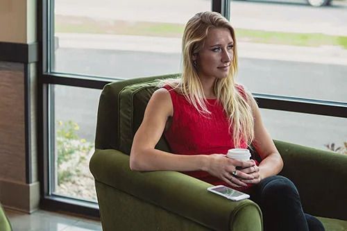 A woman is sitting in a chair holding a cup of coffee.