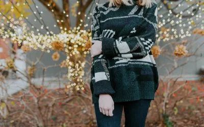 A woman in a sweater is standing in front of a tree with lights.
