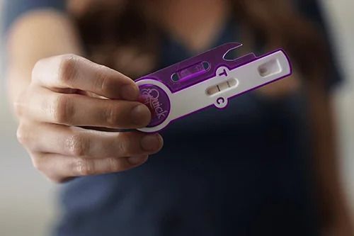 A woman is holding a pregnancy test in her hand.