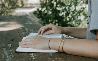 A woman is sitting at a table reading a bible.