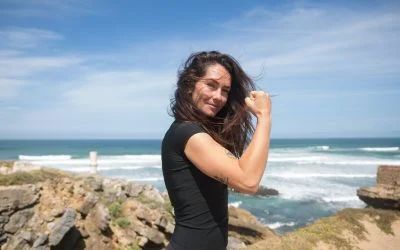 A woman in a black dress is standing on a rock near the ocean.