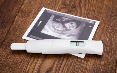 A pregnancy test is sitting on a wooden table next to an ultrasound.