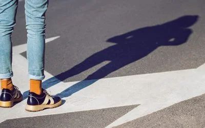 A person is standing on a street with their shadow on the ground.