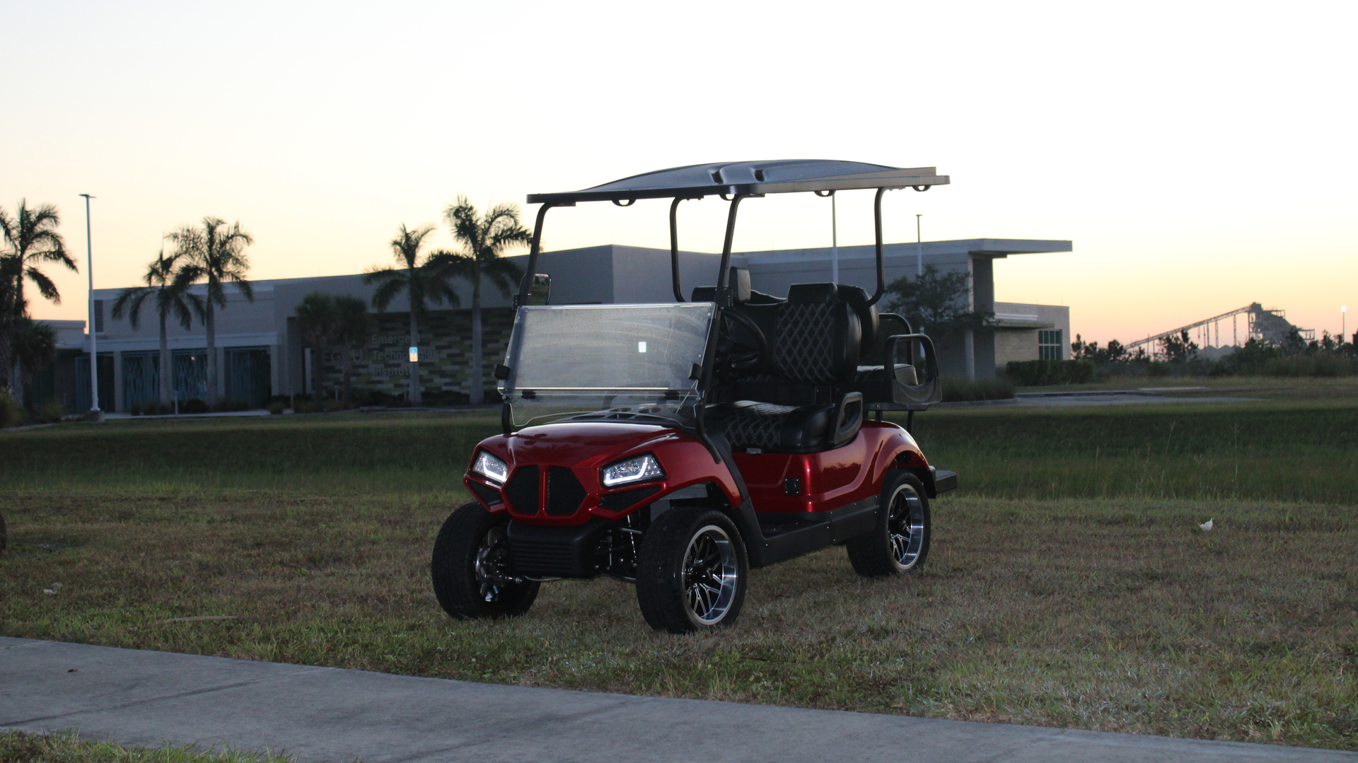 Red Motive EV golf cart with black trim, on a black and white background.