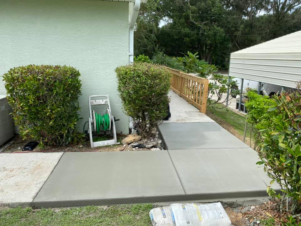 Newly poured concrete pathway next to a light green building, leading to a wooden ramp.