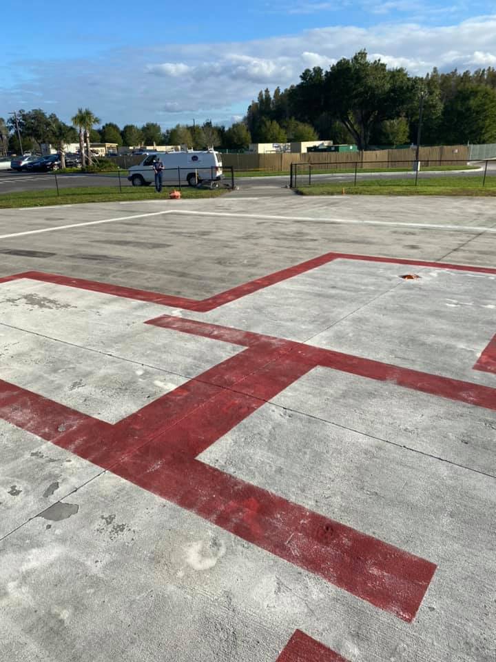 Concrete helipad with red markings; van and people in background.