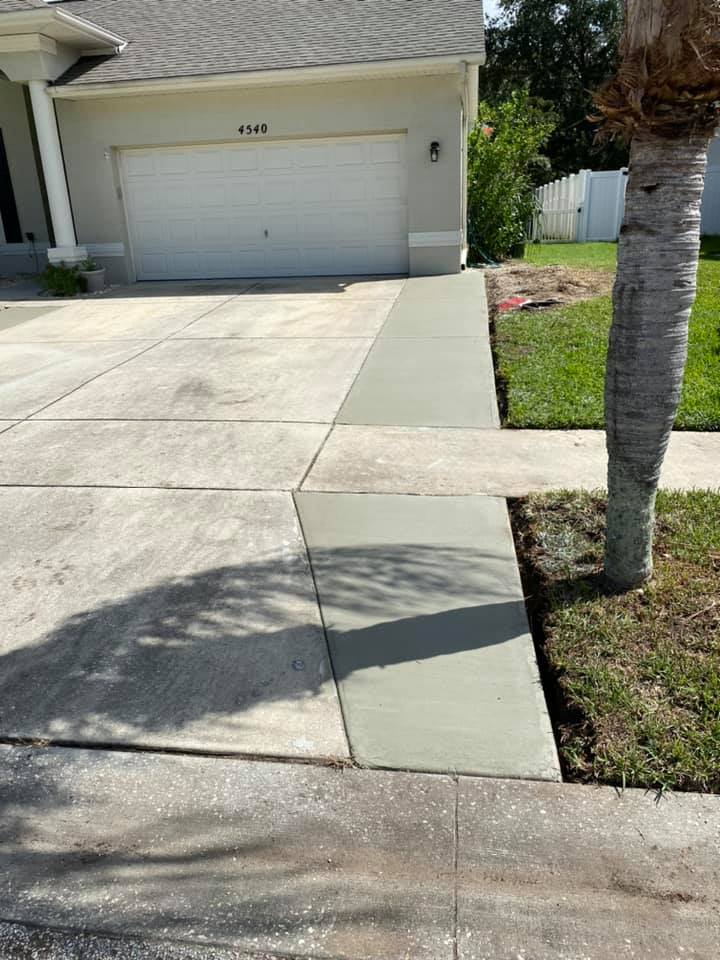 New concrete walkway next to an older concrete driveway in front of a beige house with a garage.