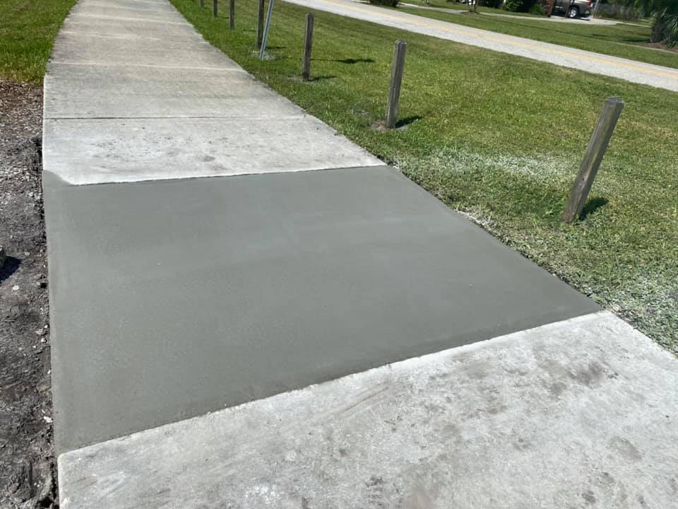Freshly poured concrete patch on a sidewalk, lighter gray than the aged surrounding concrete.