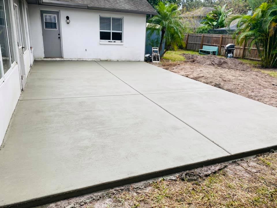 Newly poured gray concrete patio in backyard, with house in the background.