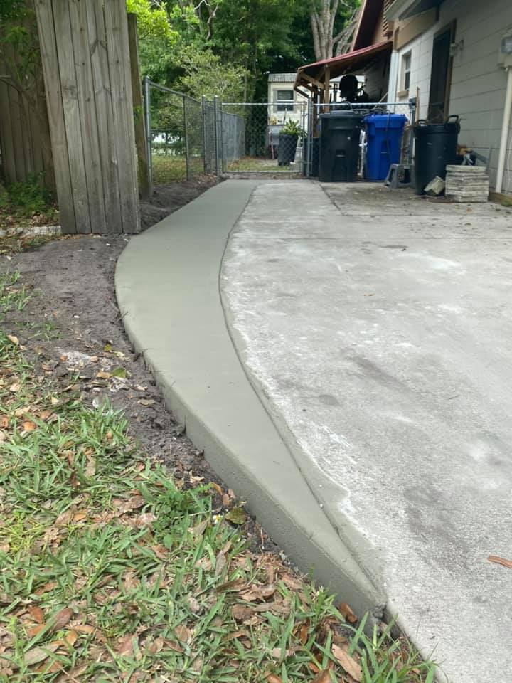 Newly poured concrete curb and walkway alongside grass and a building.