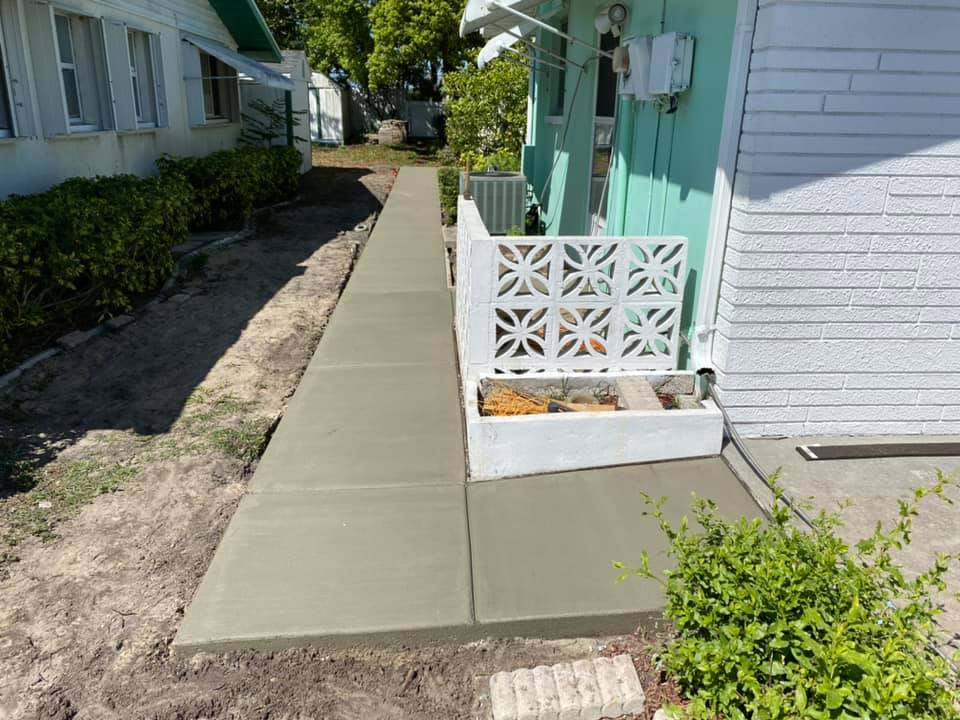 New concrete sidewalk alongside a building with a decorative white gate and small plants.