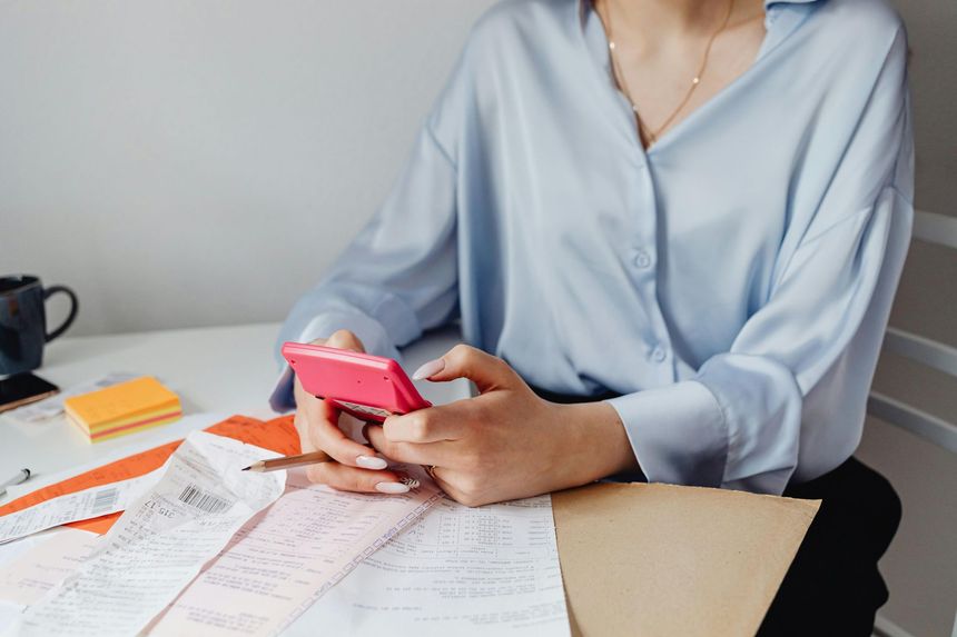 Person typing on laptop at desk with money, calculator, and papers.