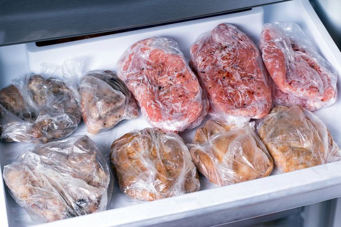 Cassetto del congelatore pieno di carne e pane sottovuoto, alcuni avvolti nella plastica.