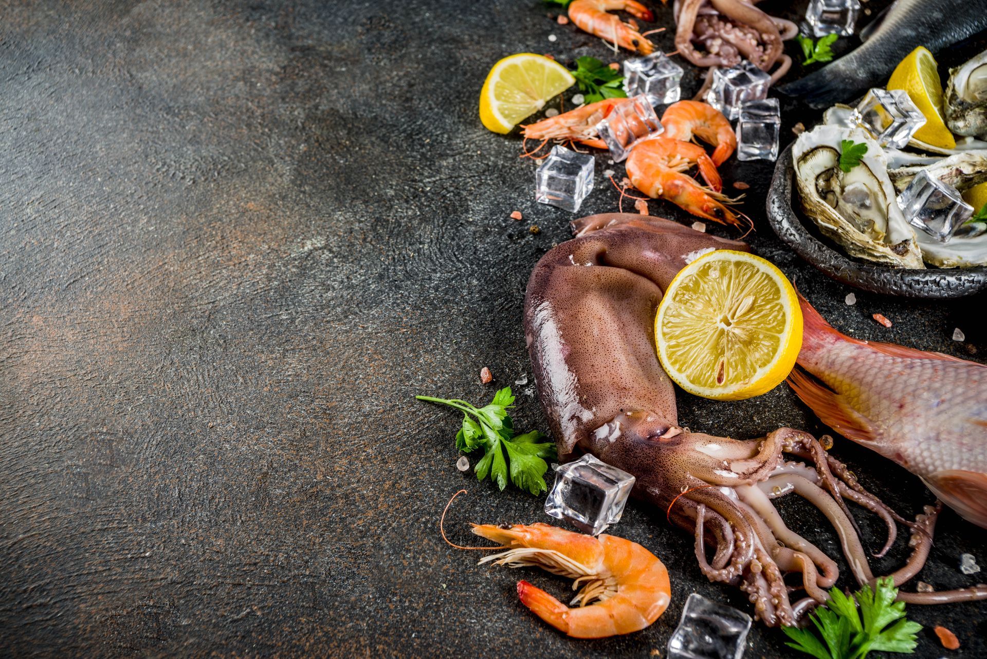 Piatto di frutti di mare con polpo, gamberi, pesce, fette di limone ed erbe aromatiche su una superficie di pietra scura.