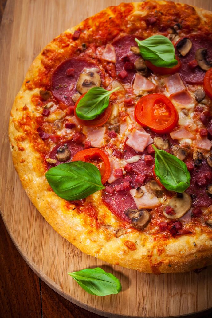Primo piano di una pizza vegetariana con foglie di basilico e pomodorini su un tagliere di legno.