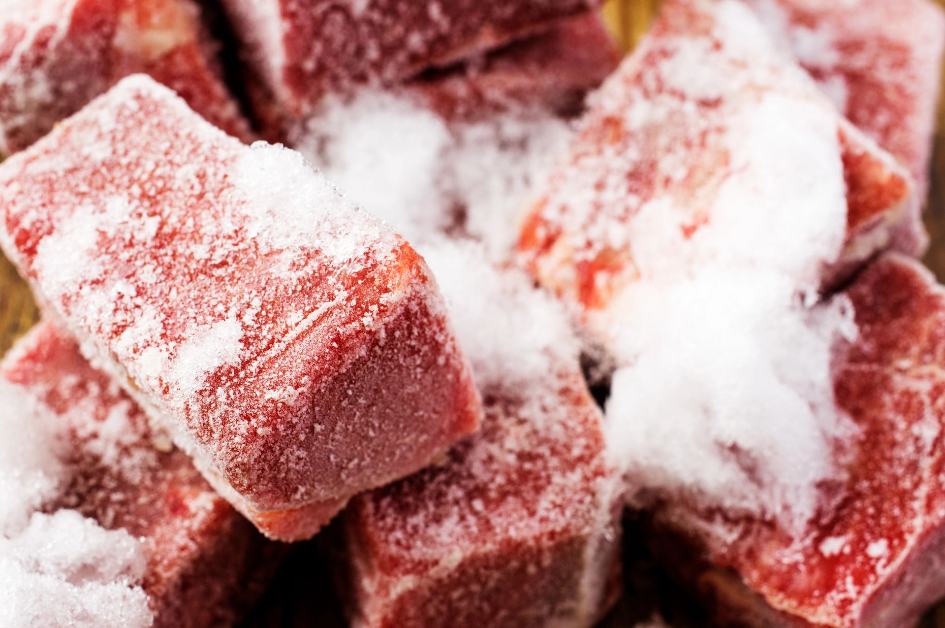 Pezzi di carne rossa ricoperti di brina, ammucchiati su un vassoio o un tagliere.