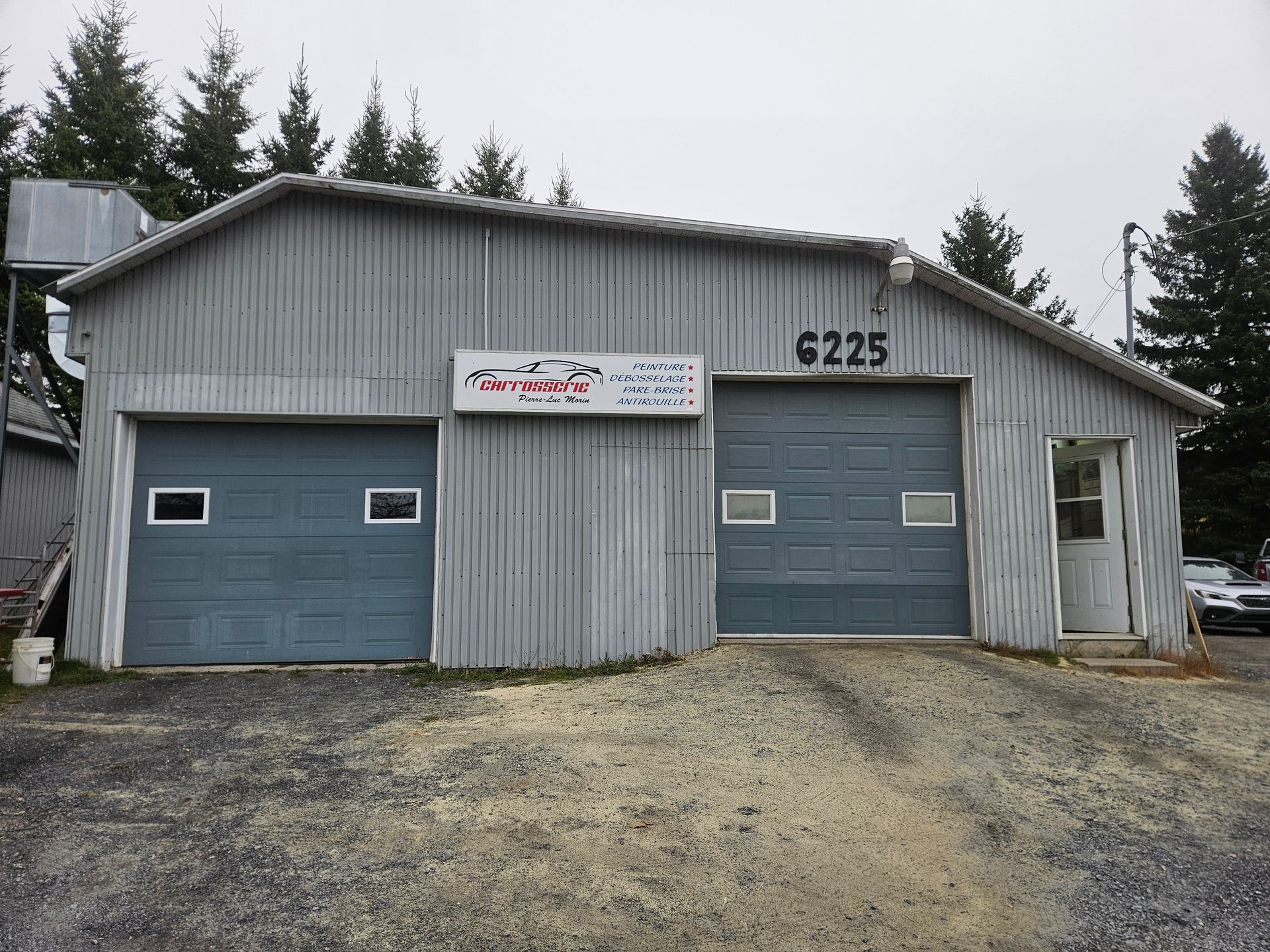 Bâtiment gris avec deux portes de garage et une petite porte, panneau au-dessus des portes indiquant « AMT Auto Repair ».