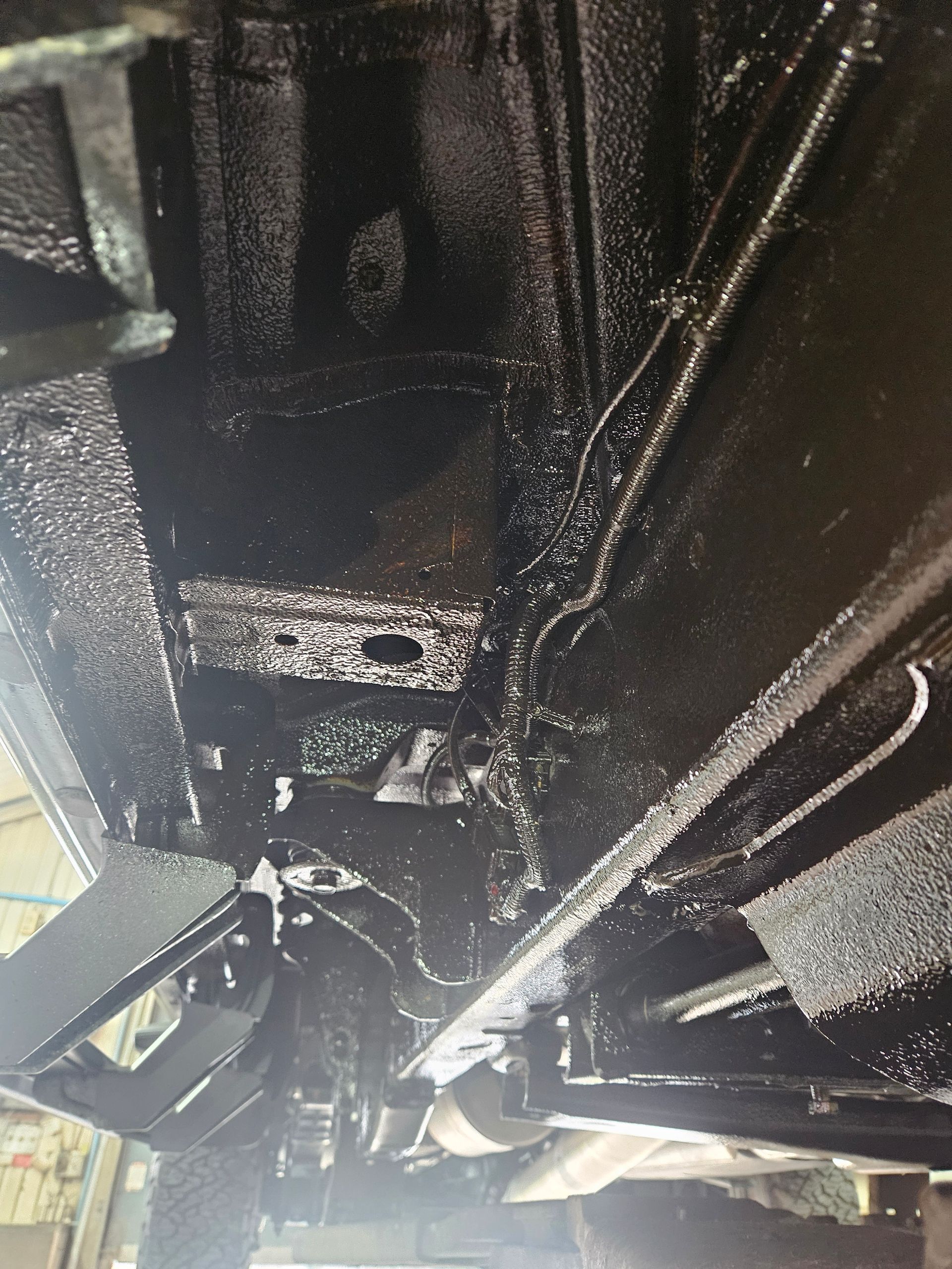 Dessous de caisse noir d'un véhicule, récemment recouvert d'un produit d'étanchéité.