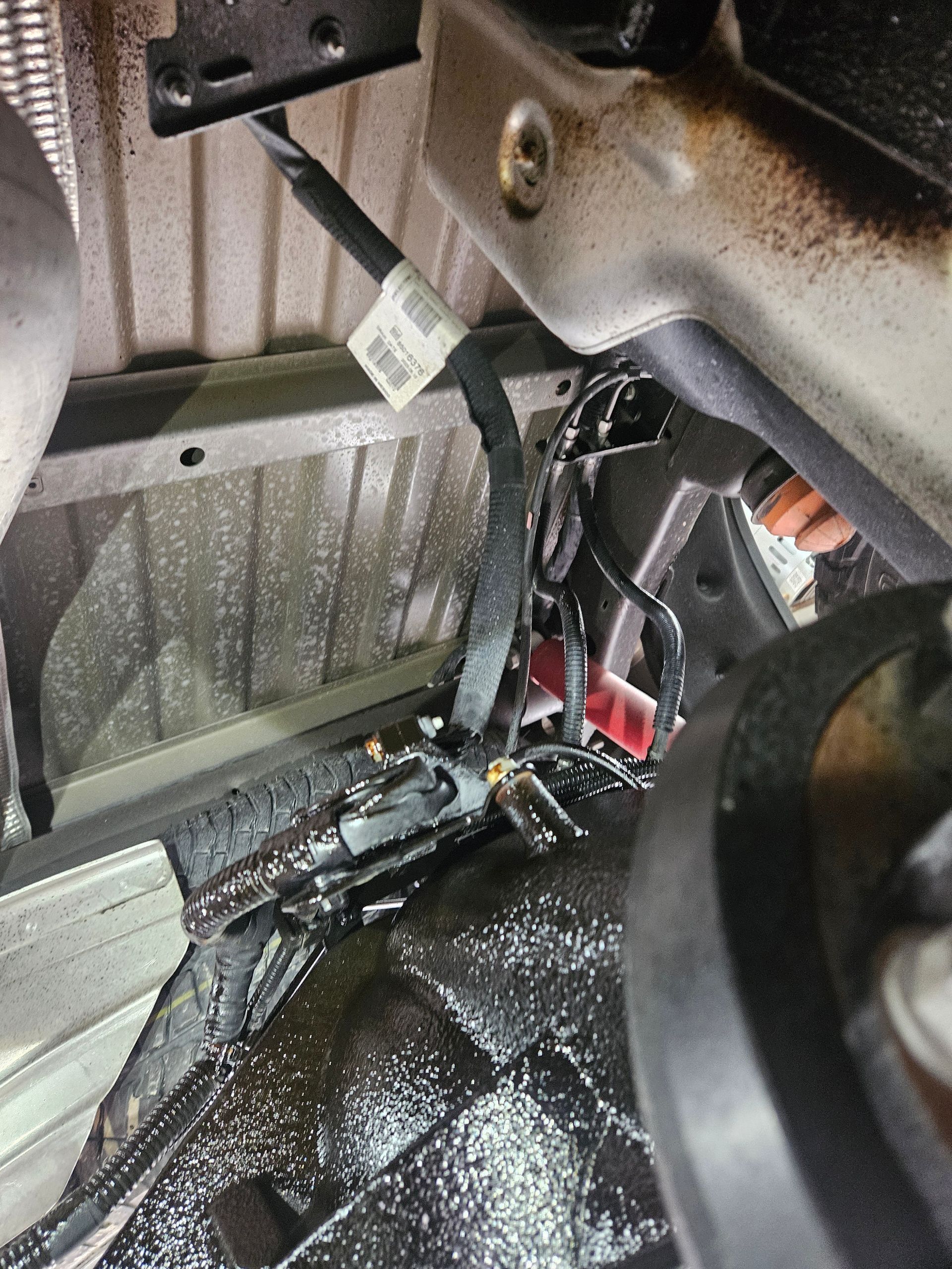 Faisceau de câbles sous le châssis. Câbles noirs, imbibés d'un liquide foncé, fixés à la tôle sous le véhicule.