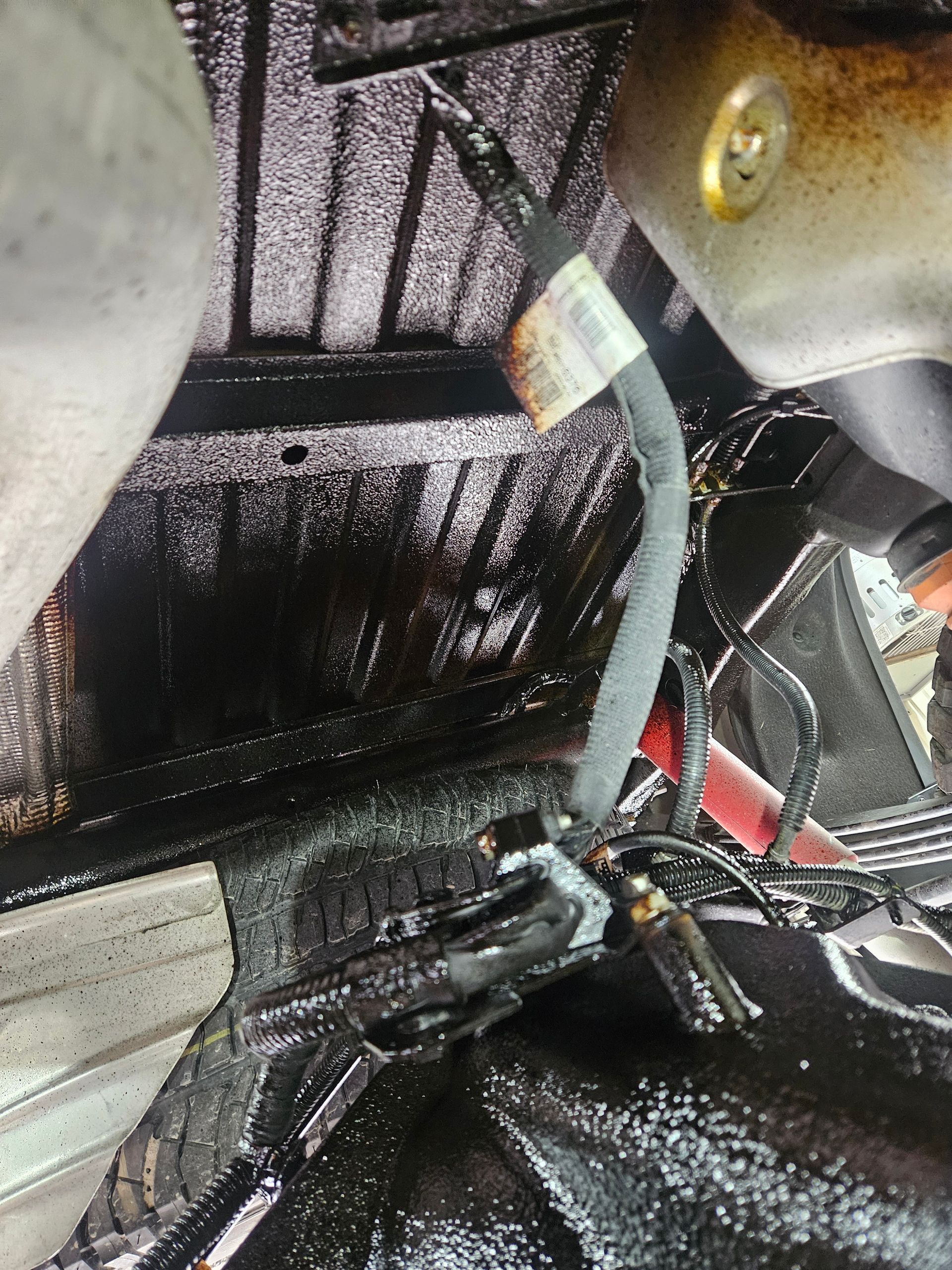 Châssis de véhicule noirci, avec un tuyau en caoutchouc foncé et un câblage fixé par des clips.