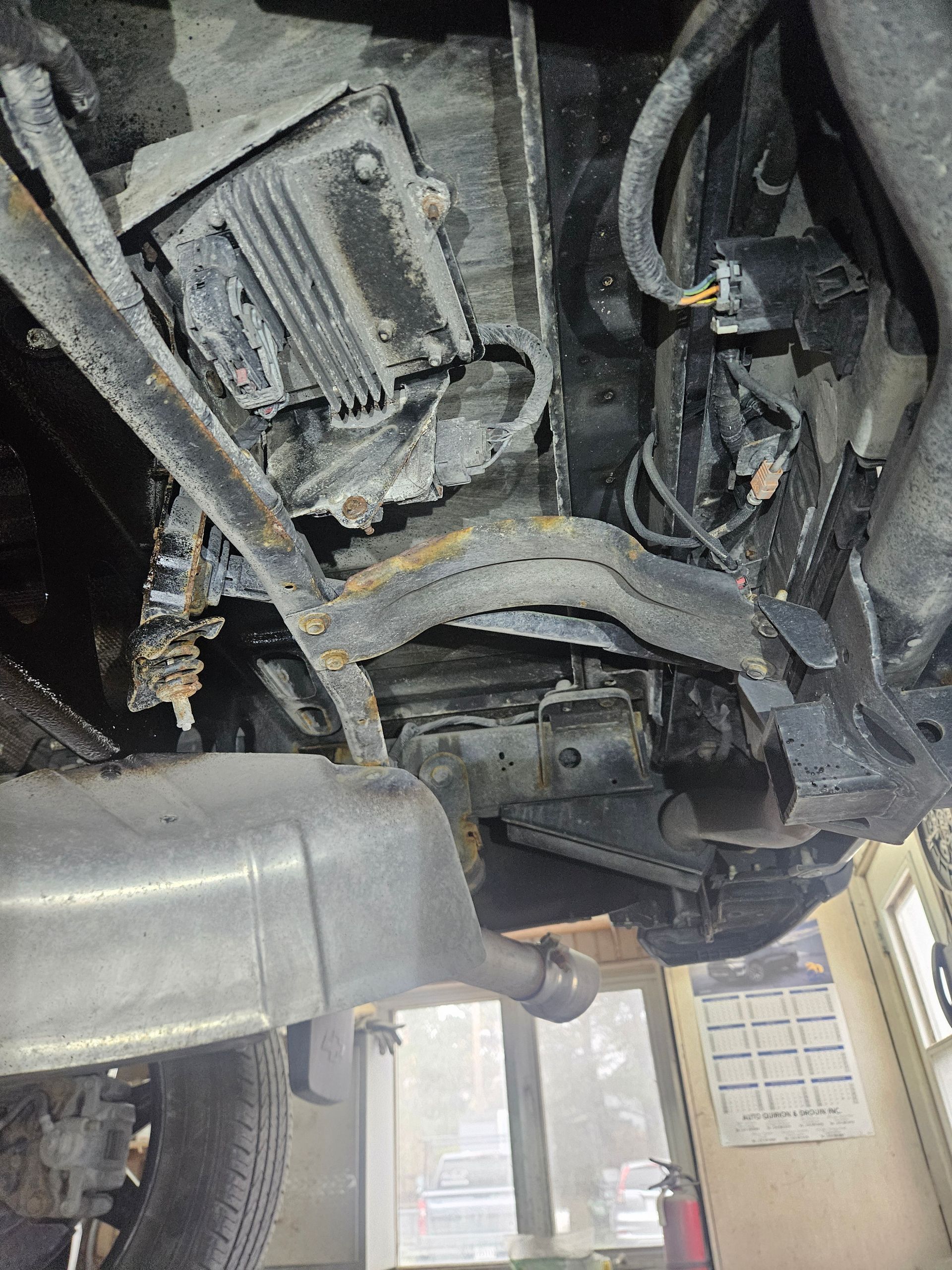 Vue du dessous d'un véhicule, montrant l'échappement, la suspension et des composants rouillé et de corrodé.