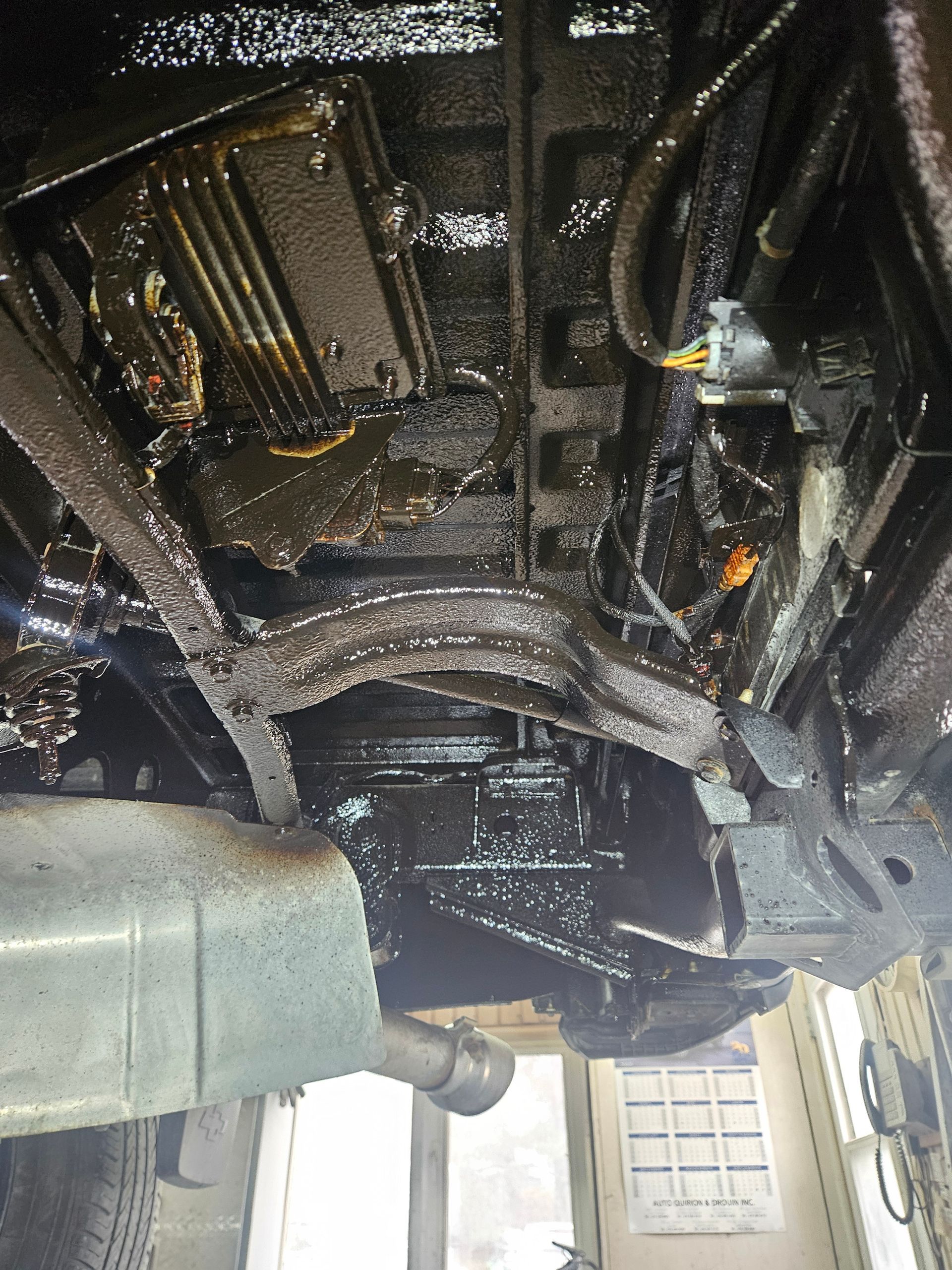 Dessous de véhicule recouvert d'une épaisse couche d'huile foncée, avec un pot d'échappement visible.