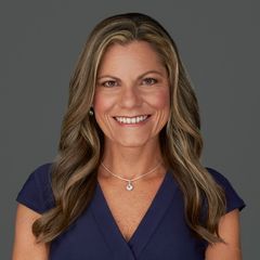 A woman is sitting at a desk with a laptop and a vase of flowers.