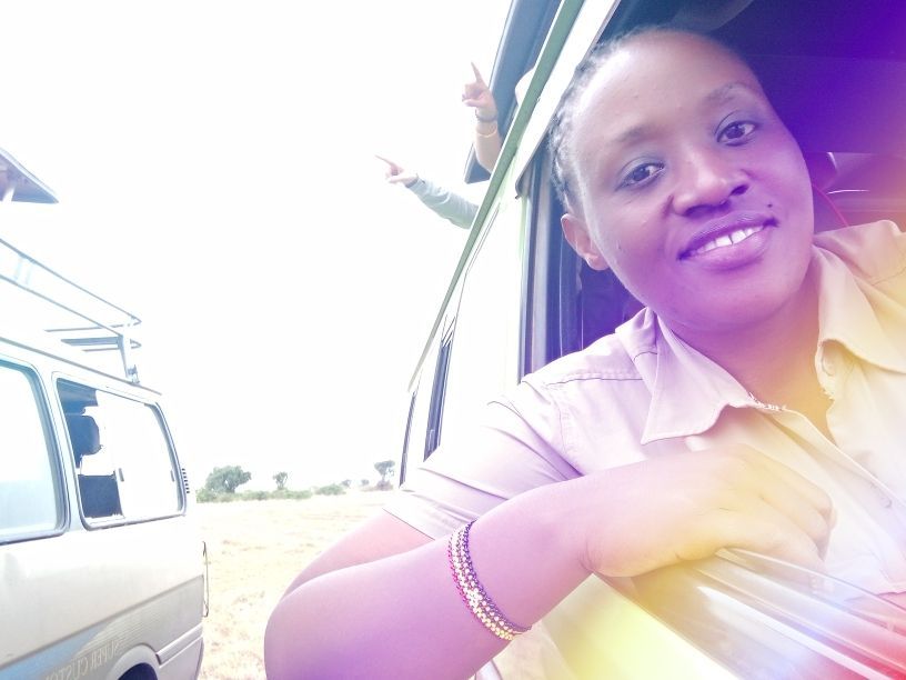 Woman leaning out of a vehicle window, smiling. Sunlight.
