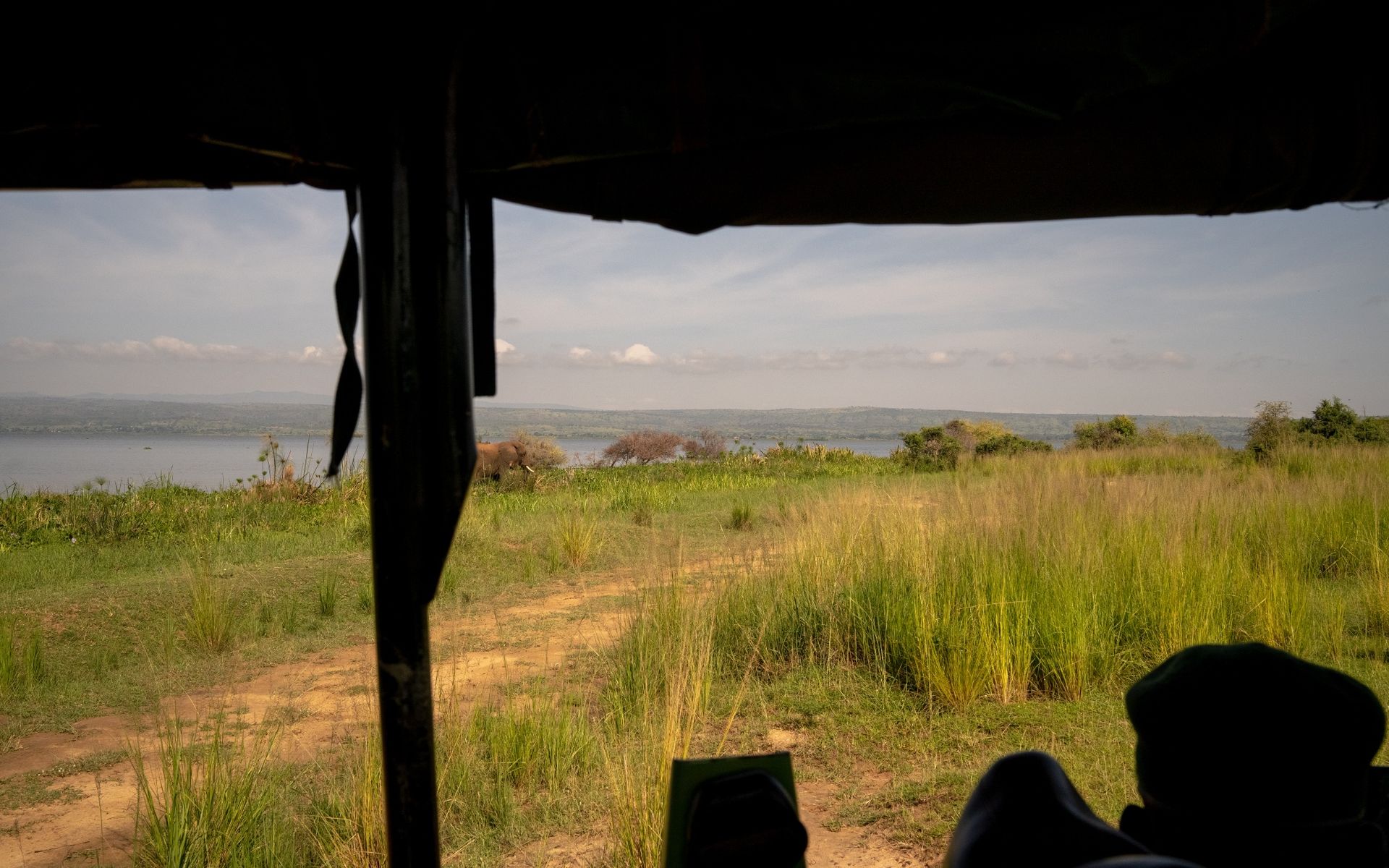 View from inside a vehicle overlooking a grassy plain and body of water under a cloudy sky.
