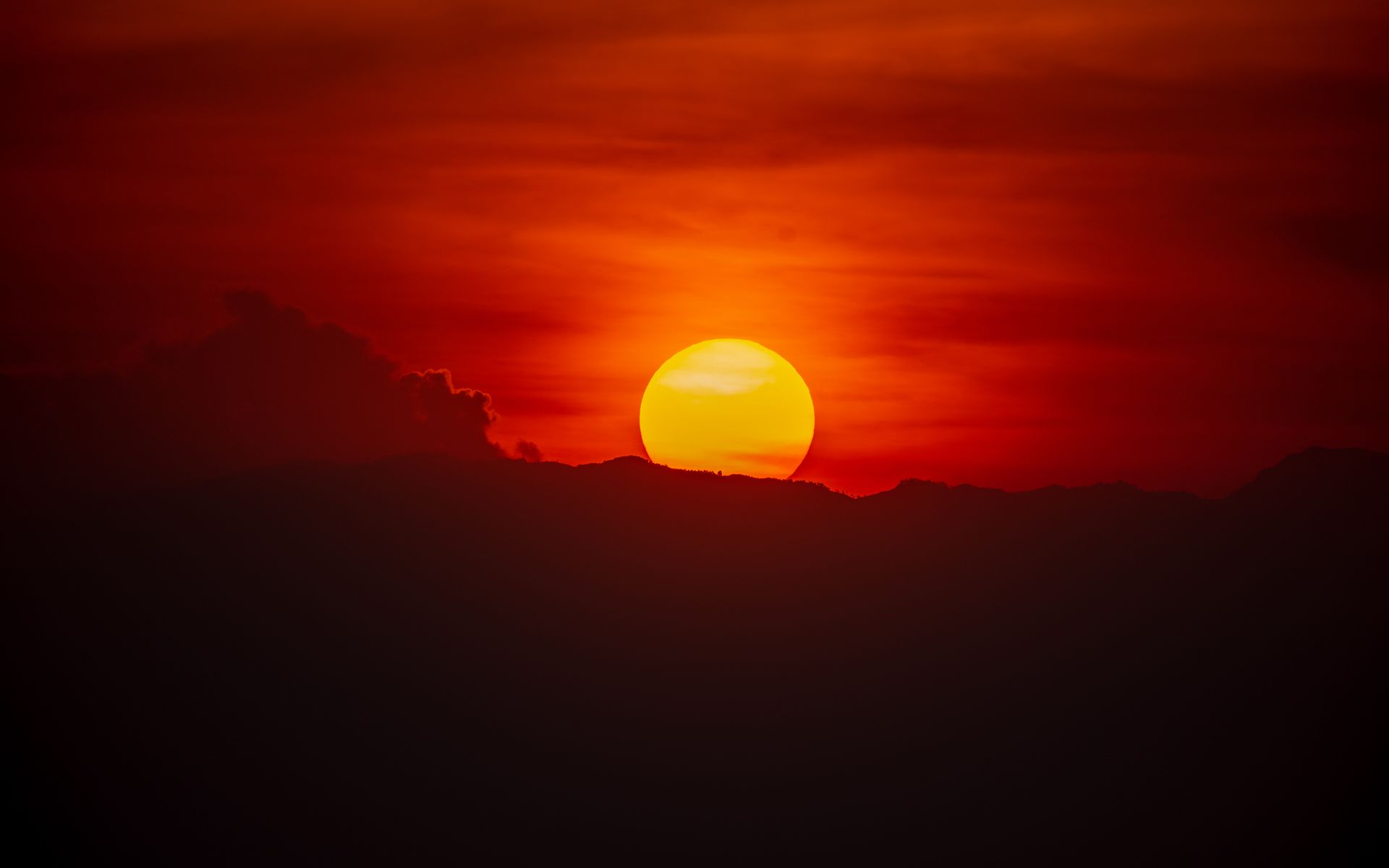 Fiery sunset with a large, yellow sun partially obscured by dark, silhouetted clouds.