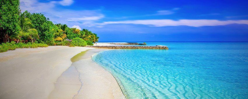 A tropical beach with white sand, turquoise water, and lush green trees under a blue sky.