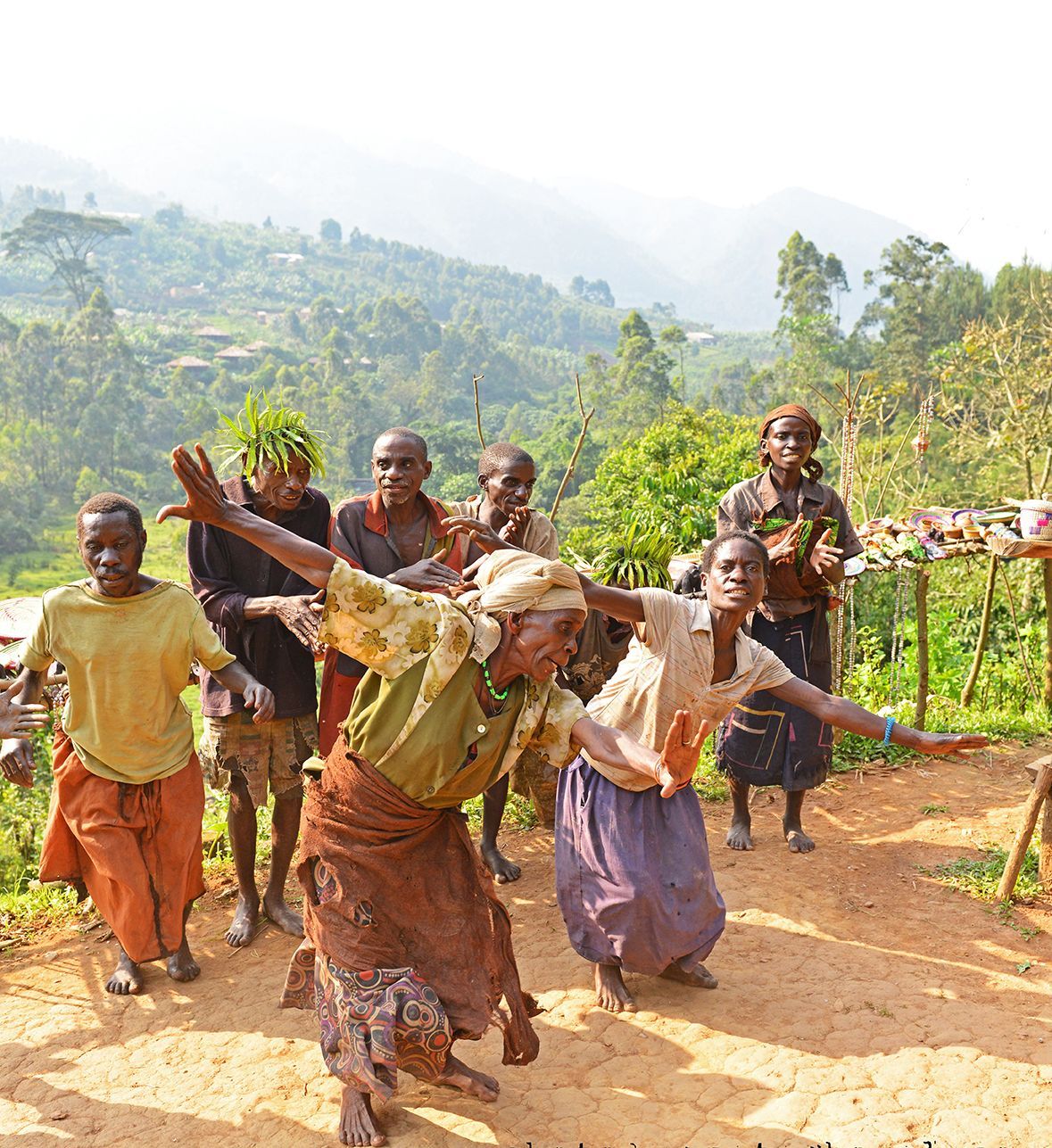 Group of people dancing outdoors in front of a hilly, green backdrop. They are celebrating and look excited.
