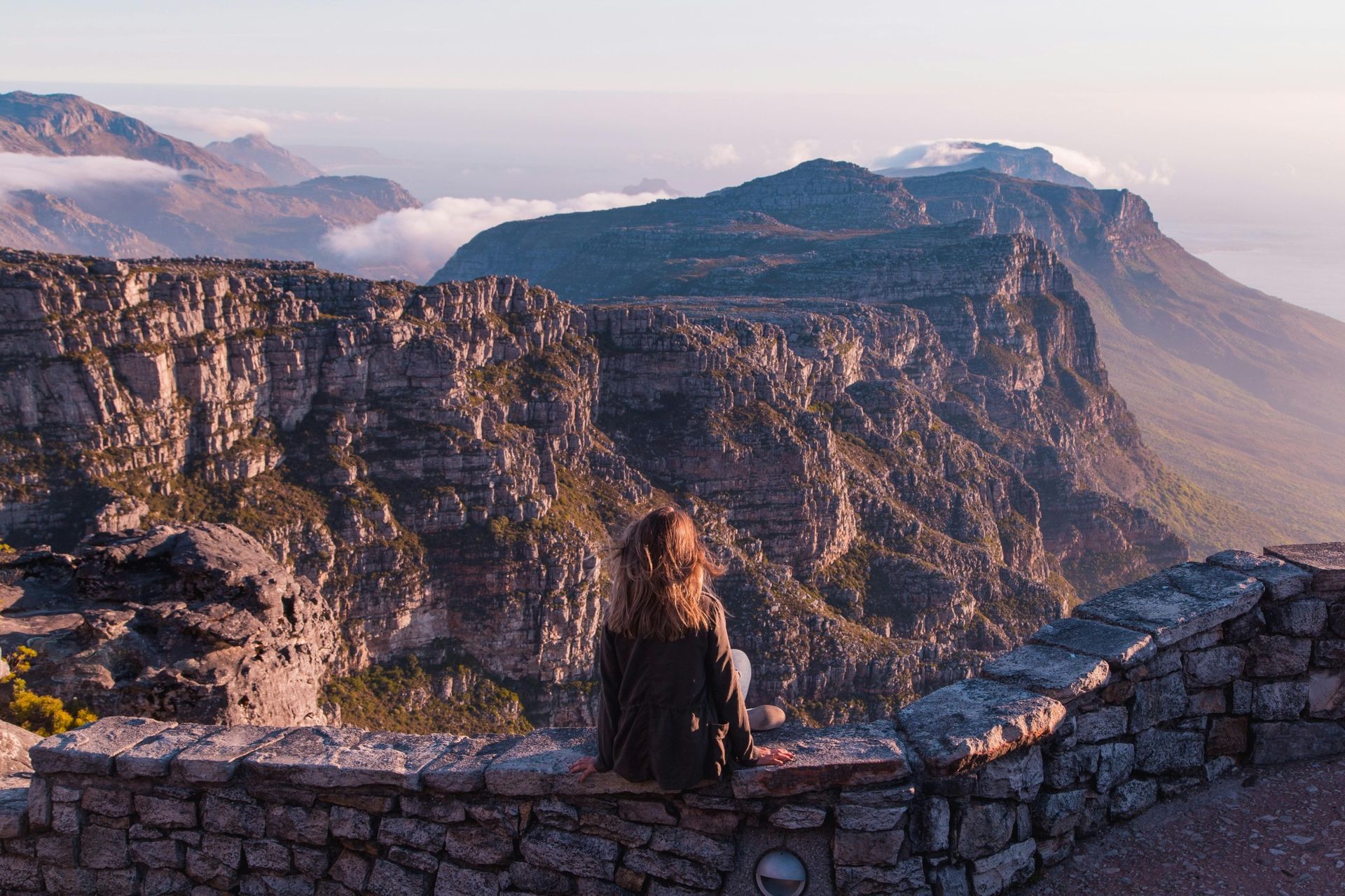 Woman overlooking mountain range from stone wall. Soft light, scenic view.