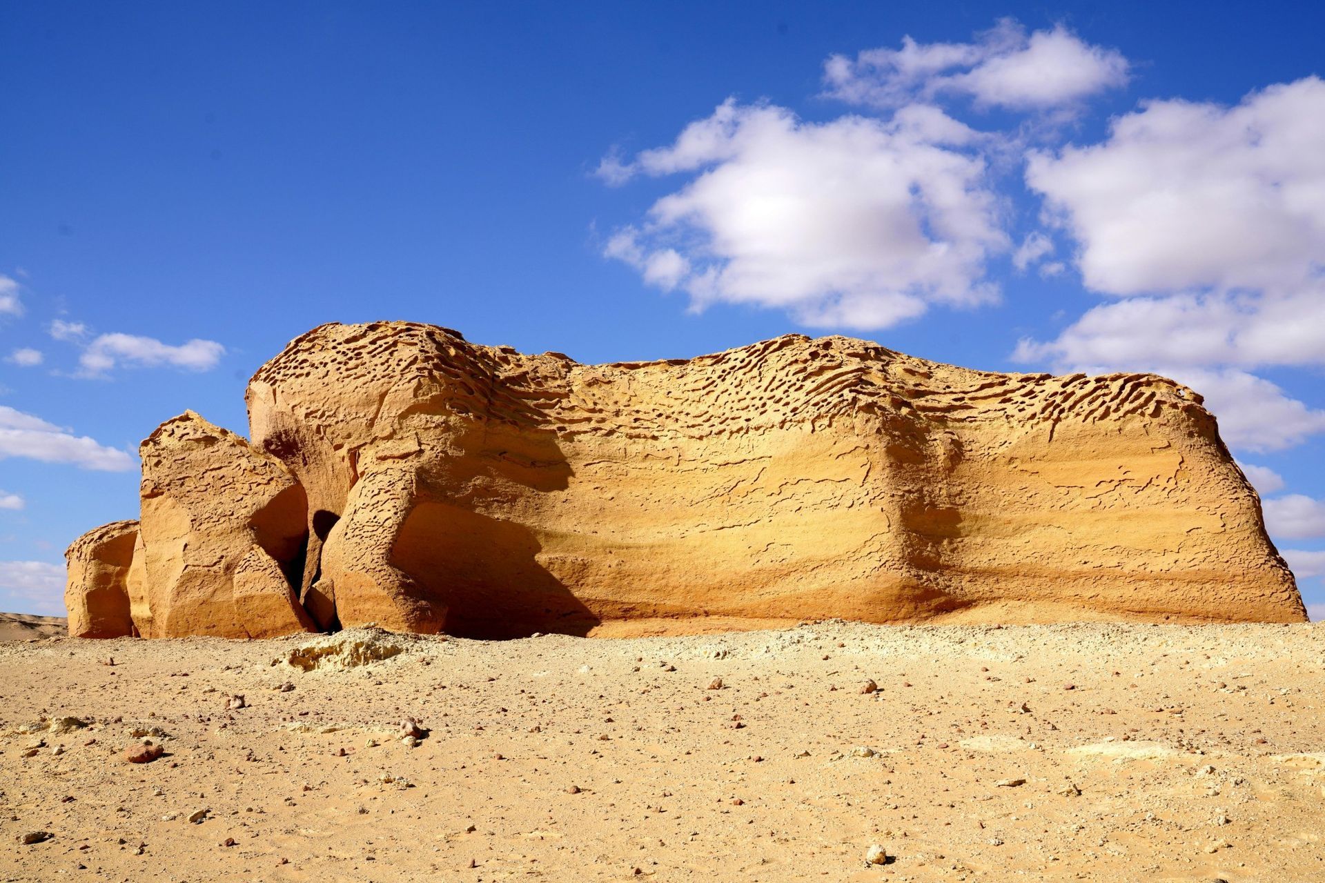 Sandstone rock formation in desert landscape under a blue sky with scattered clouds.