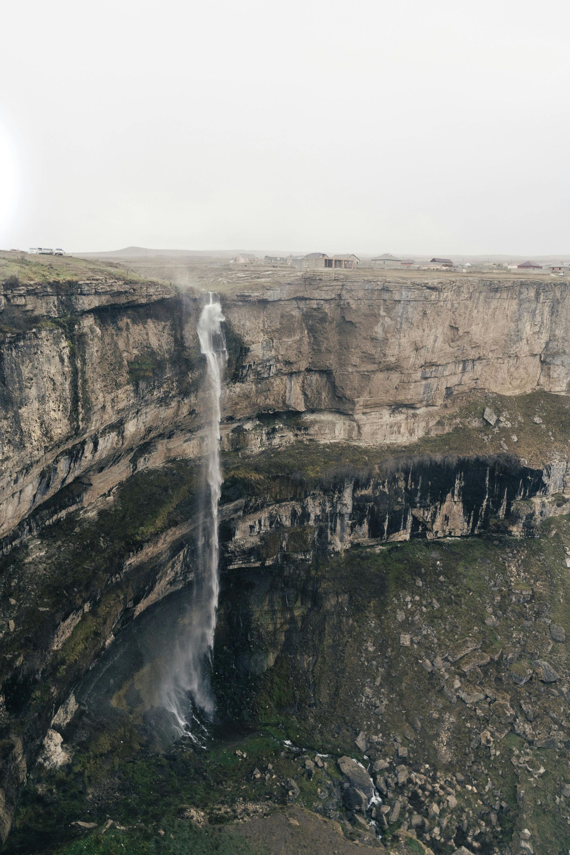 Waterfall cascading over a rocky cliffside, with a foggy sky in the background.
