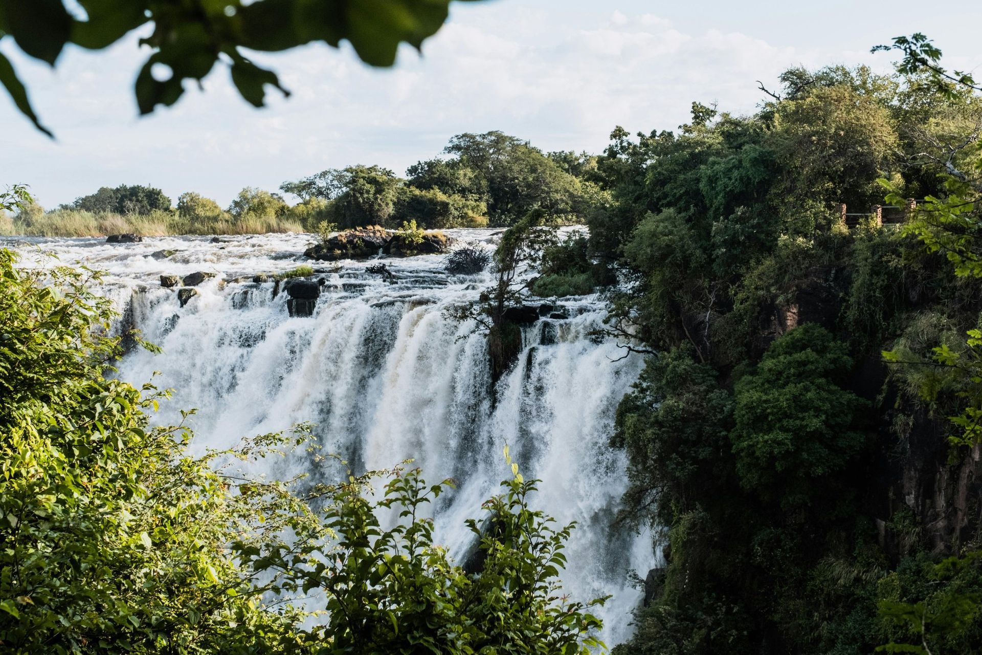 Waterfall cascading over rocky cliffs, surrounded by lush green trees.