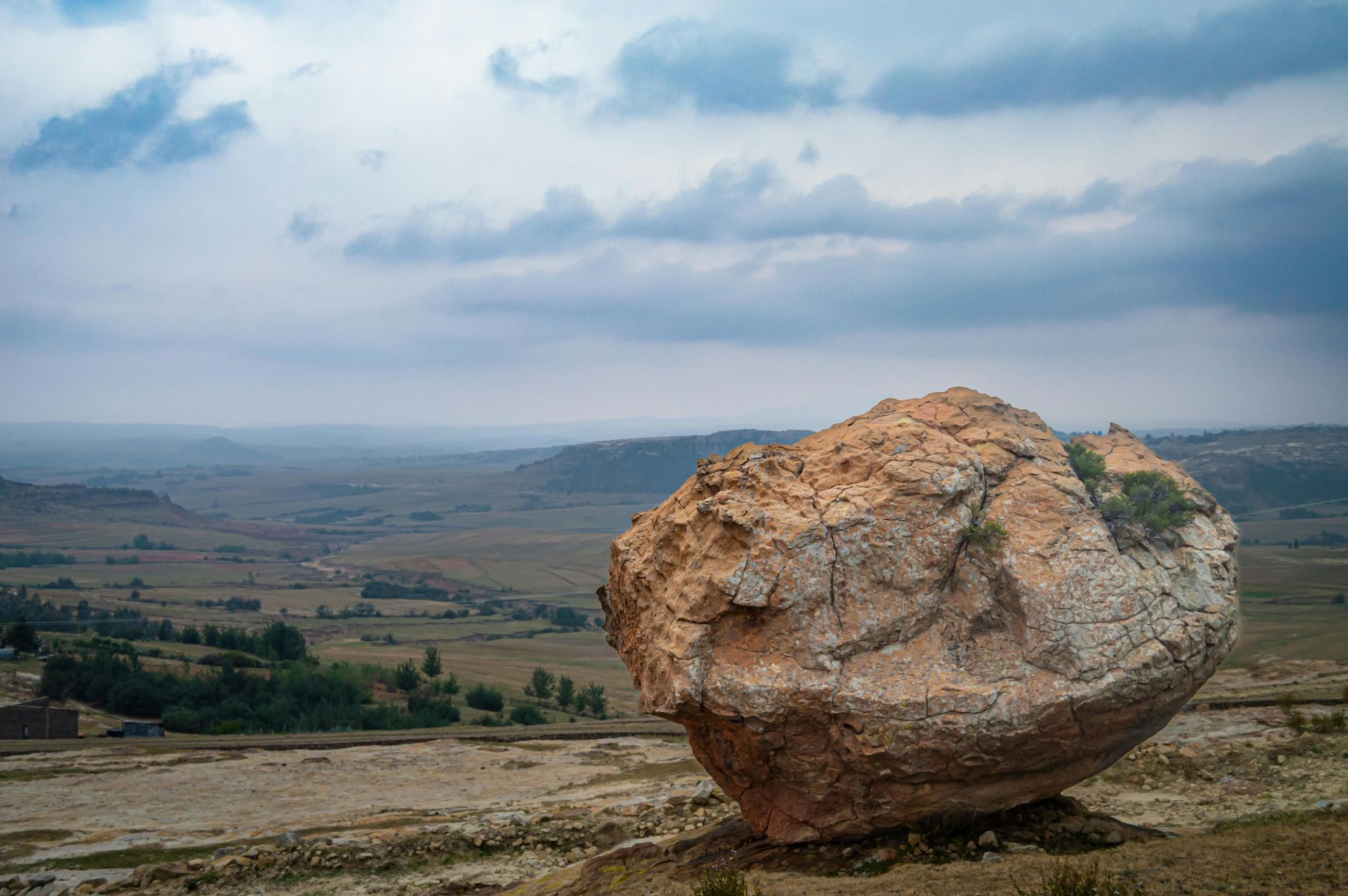 Large, rounded rock on a grassy hill overlooking a valley under a cloudy sky.