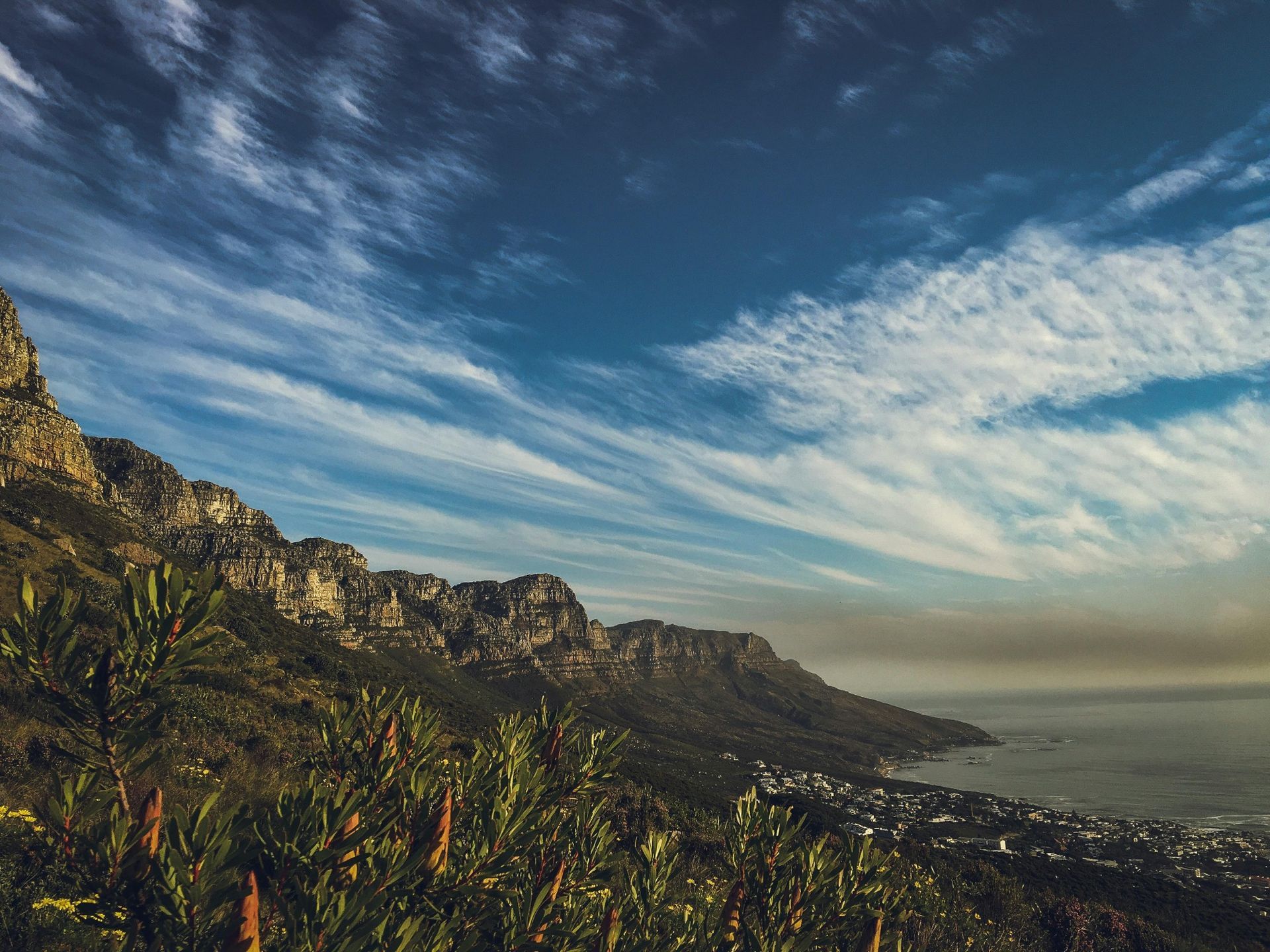 Mountains overlook a coastal town under a blue sky with streaky white clouds.