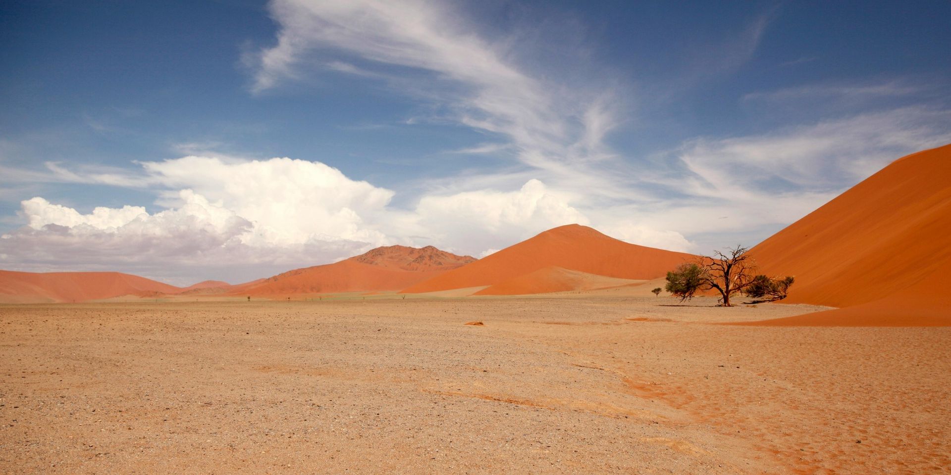 Desert landscape with orange sand dunes, blue sky, and a few scattered clouds.