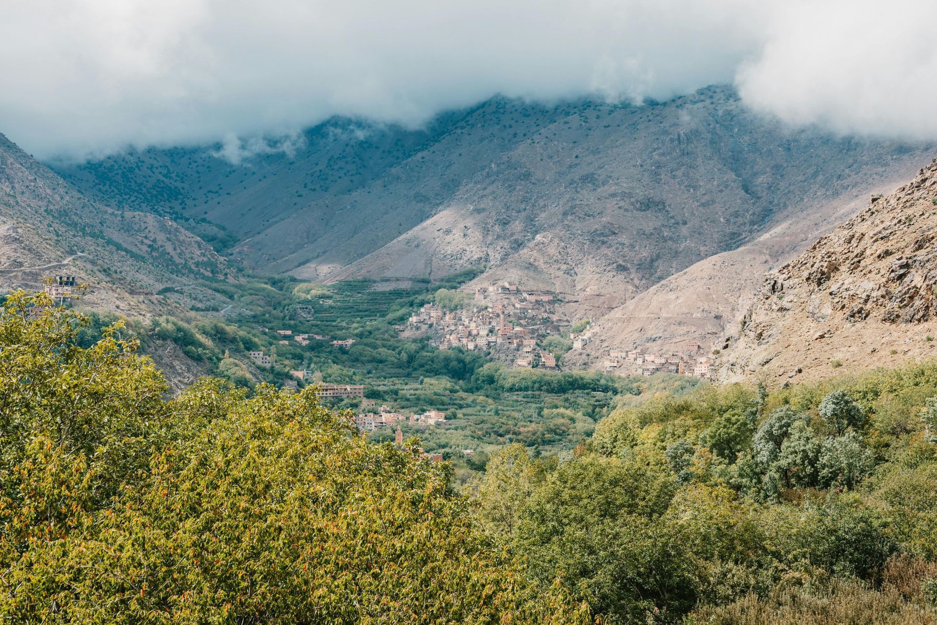 Valley with lush greenery between rocky mountains, partially obscured by clouds.