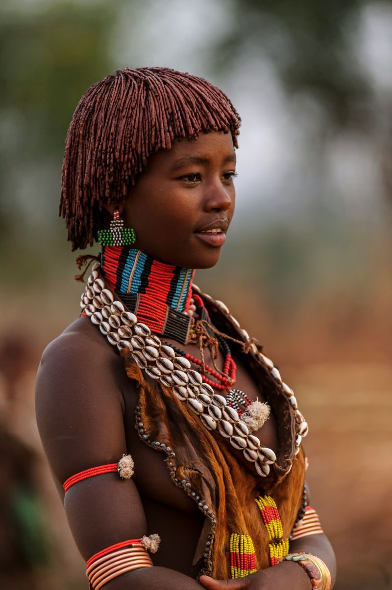 Young Hamer woman in Ethiopia, adorned with beaded jewelry and traditional hairstyle, gazing sideways.