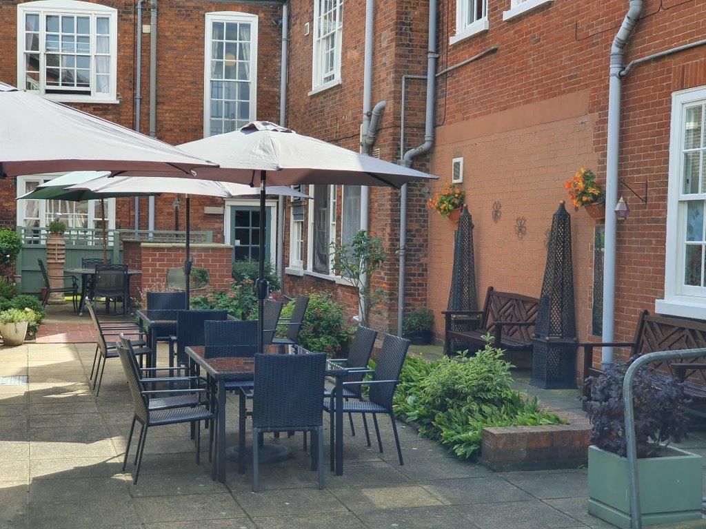 A patio with tables and chairs and umbrellas in front of a brick building.