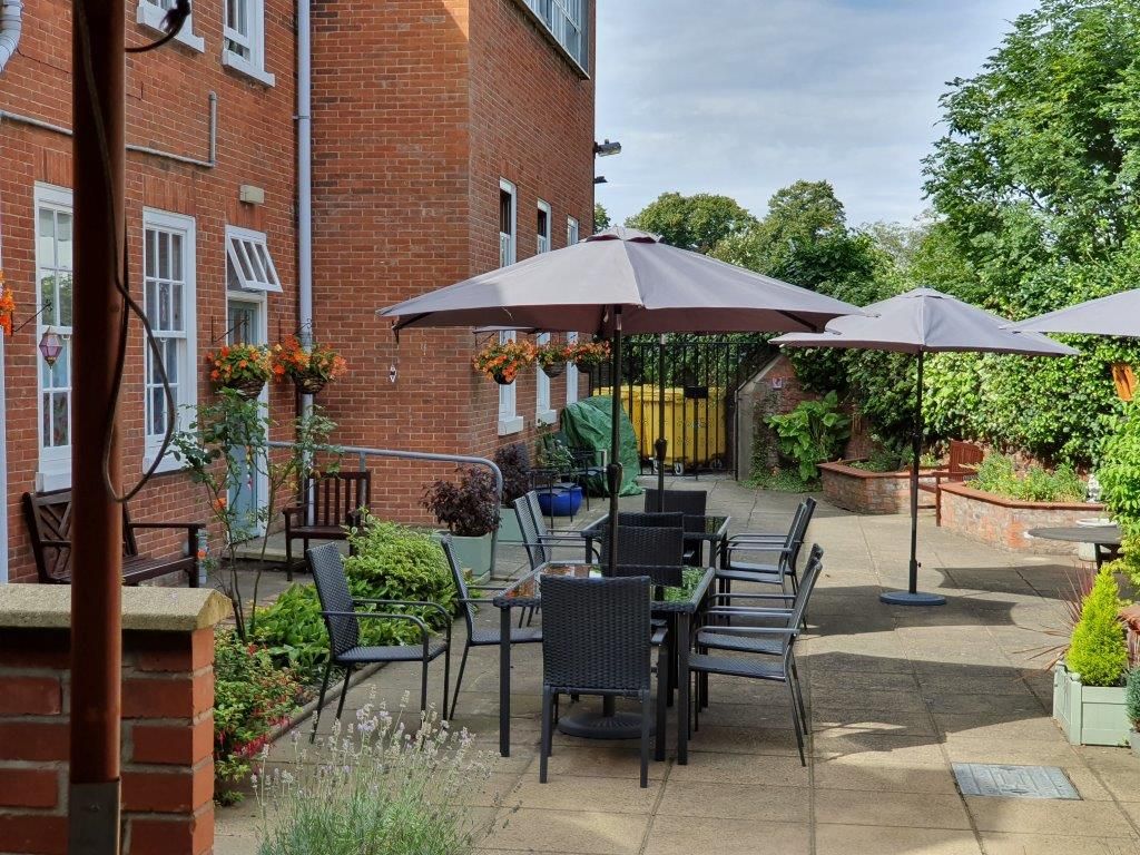 A patio with tables and chairs and umbrellas in front of a brick building.