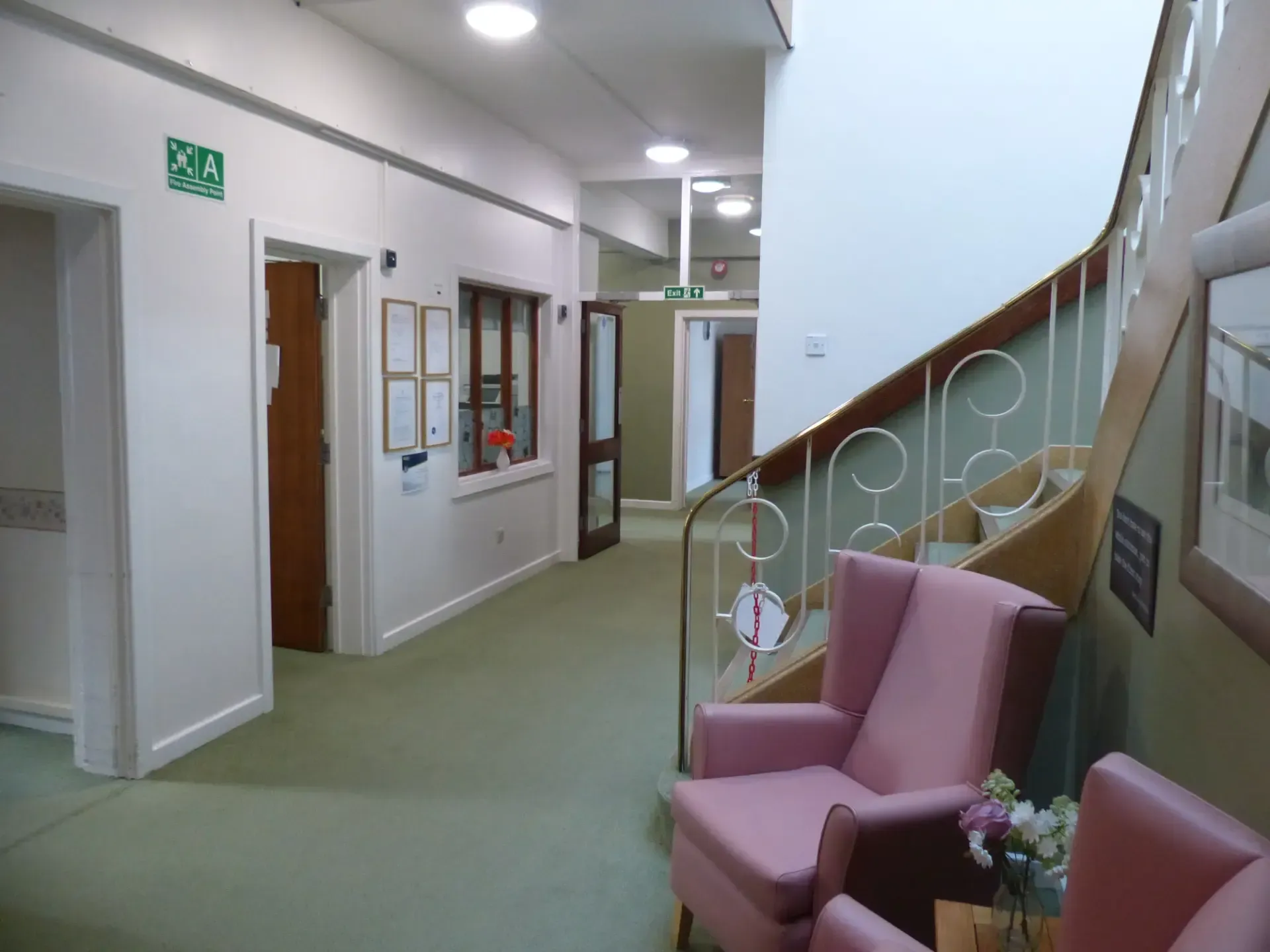 A hallway with pink chairs and a green exit sign on the wall