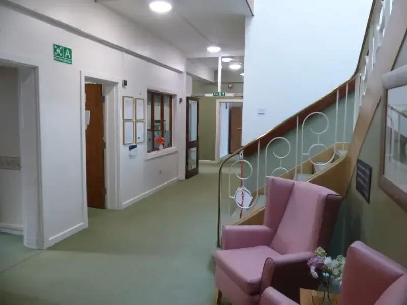 A hallway with pink chairs and a green exit sign