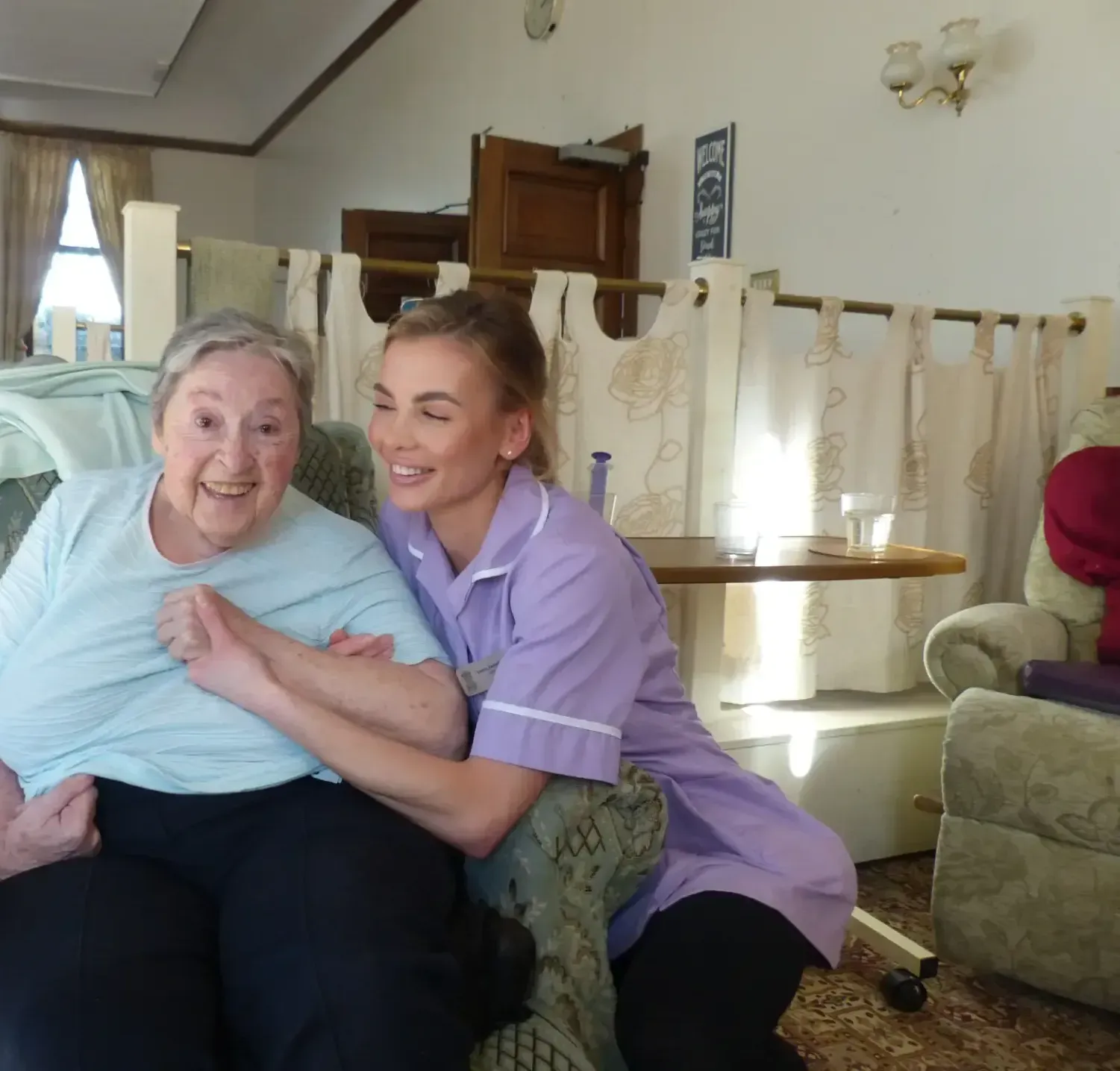 A woman in a purple shirt is hugging an older woman on a couch