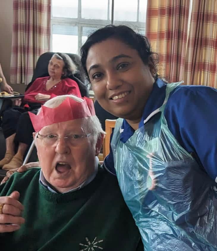 A woman is standing next to an older man wearing a paper crown